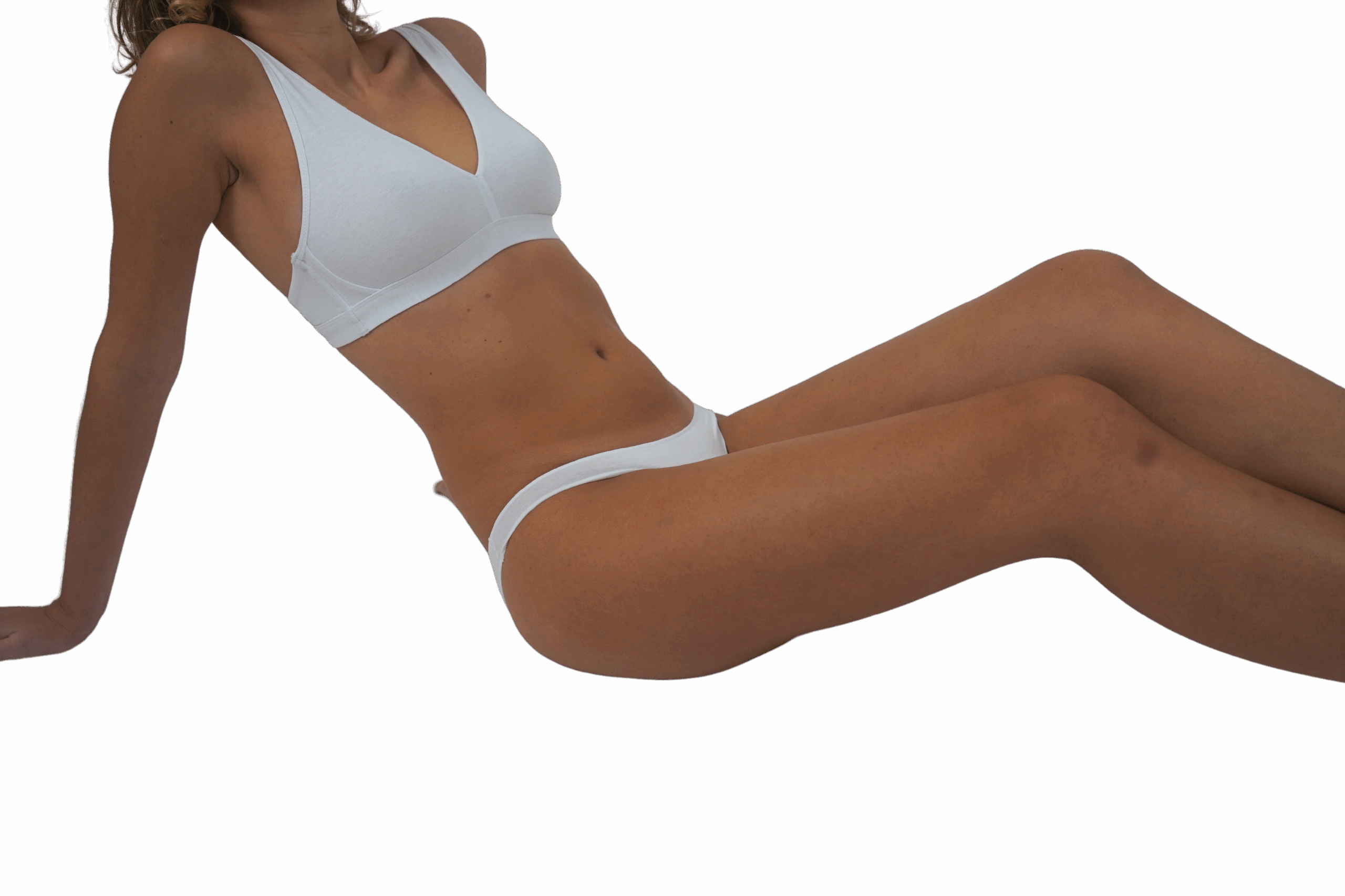 Une personne en soutien-gorge et culotte blancs est assise, les jambes étendues, un bras soutenant son corps par derrière. Le fond noir crée un contraste saisissant avec la tenue blanche. Le visage de la personne n'est pas visible sur l'image.