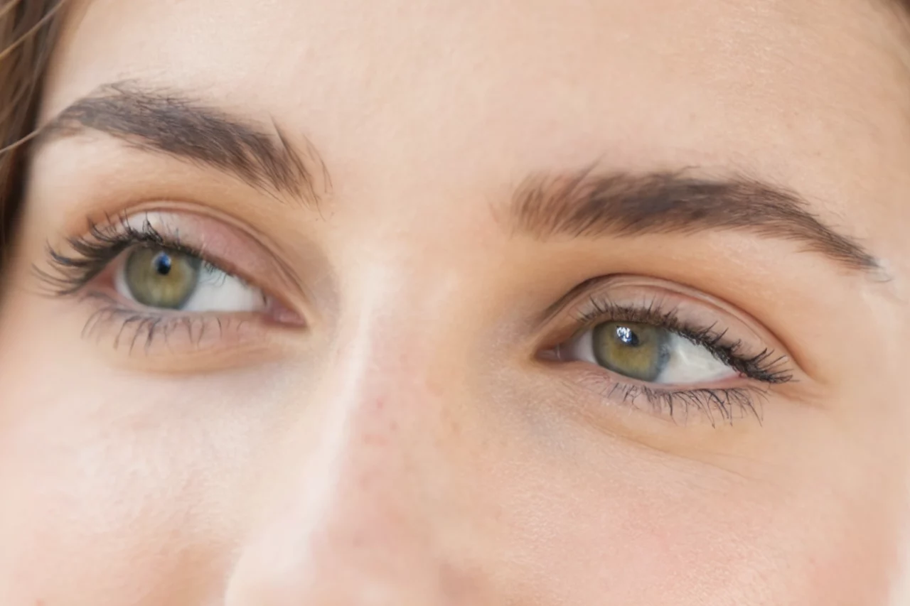 Gros plan sur les yeux d'une personne regardant de côté. Les yeux sont verts, avec de longs cils et des sourcils bien dessinés. La peau paraît lisse, révélant un teint naturel.