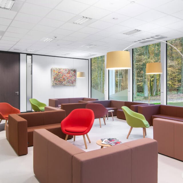 Salle d'attente lumineuse avec fauteuils colorés et vue sur la nature extérieure.