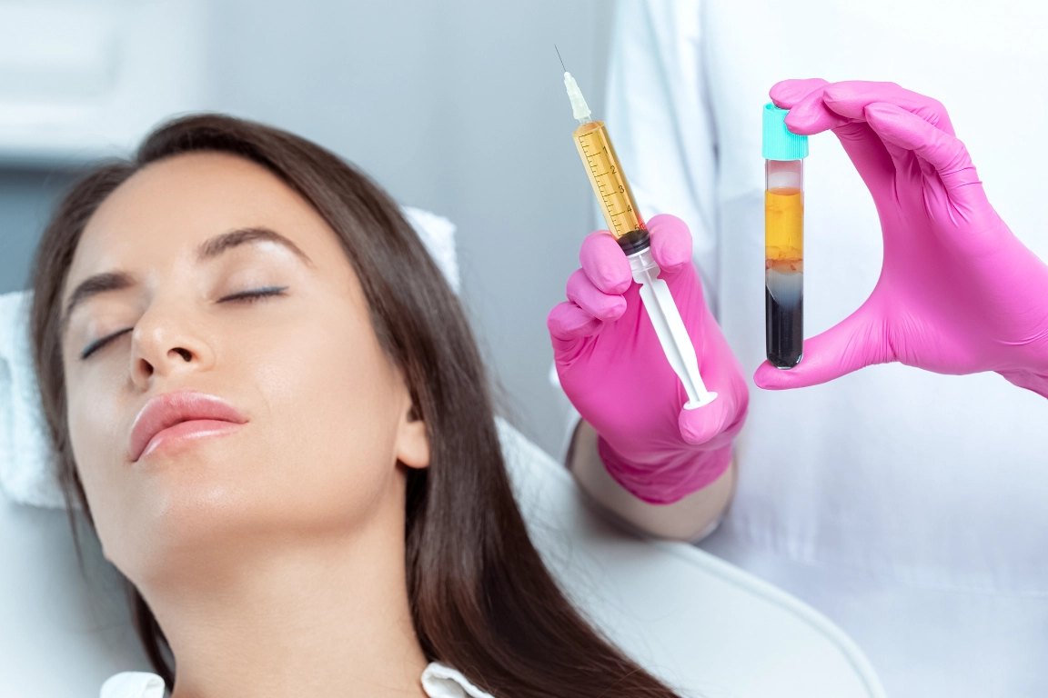 A woman with closed eyes is lying down while a person wearing pink gloves holds a syringe and a vial containing separated blood components, preparing for a medical or cosmetic procedure.