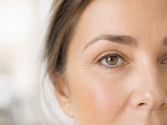 Gros plan sur le visage d'une femme montrant son œil droit, son sourcil, ainsi qu'une partie de son nez et de sa joue. La peau semble lisse, avec quelques ridules, et l'arrière-plan est légèrement flou.