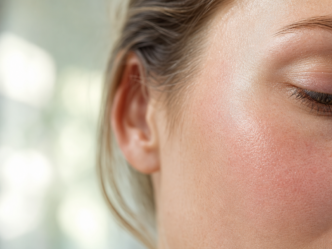 Gros plan sur le profil d'un visage, montrant une peau lisse et éclatante, un œil fermé orné de cils, un sourcil et une partie de l'oreille, la lumière naturelle mettant en valeur la texture de la peau.
